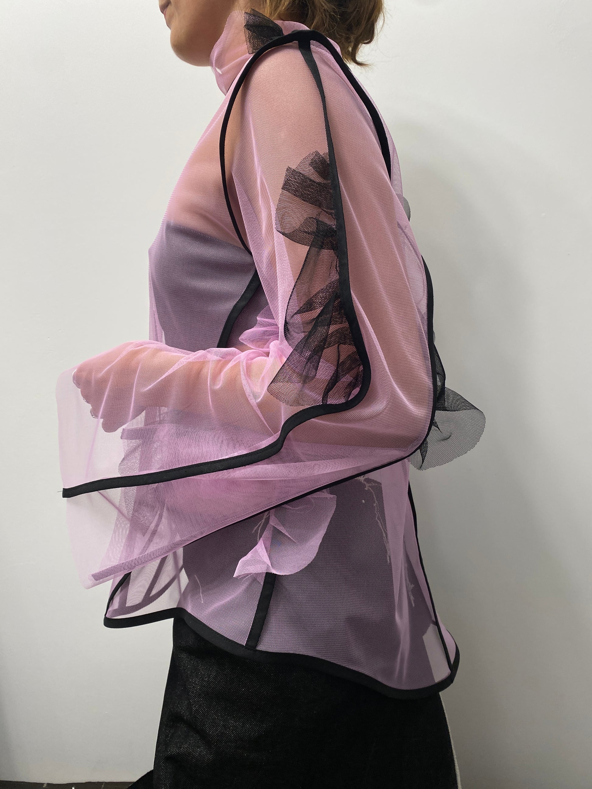 Person wearing a pink sheer garment with black trim on a white background