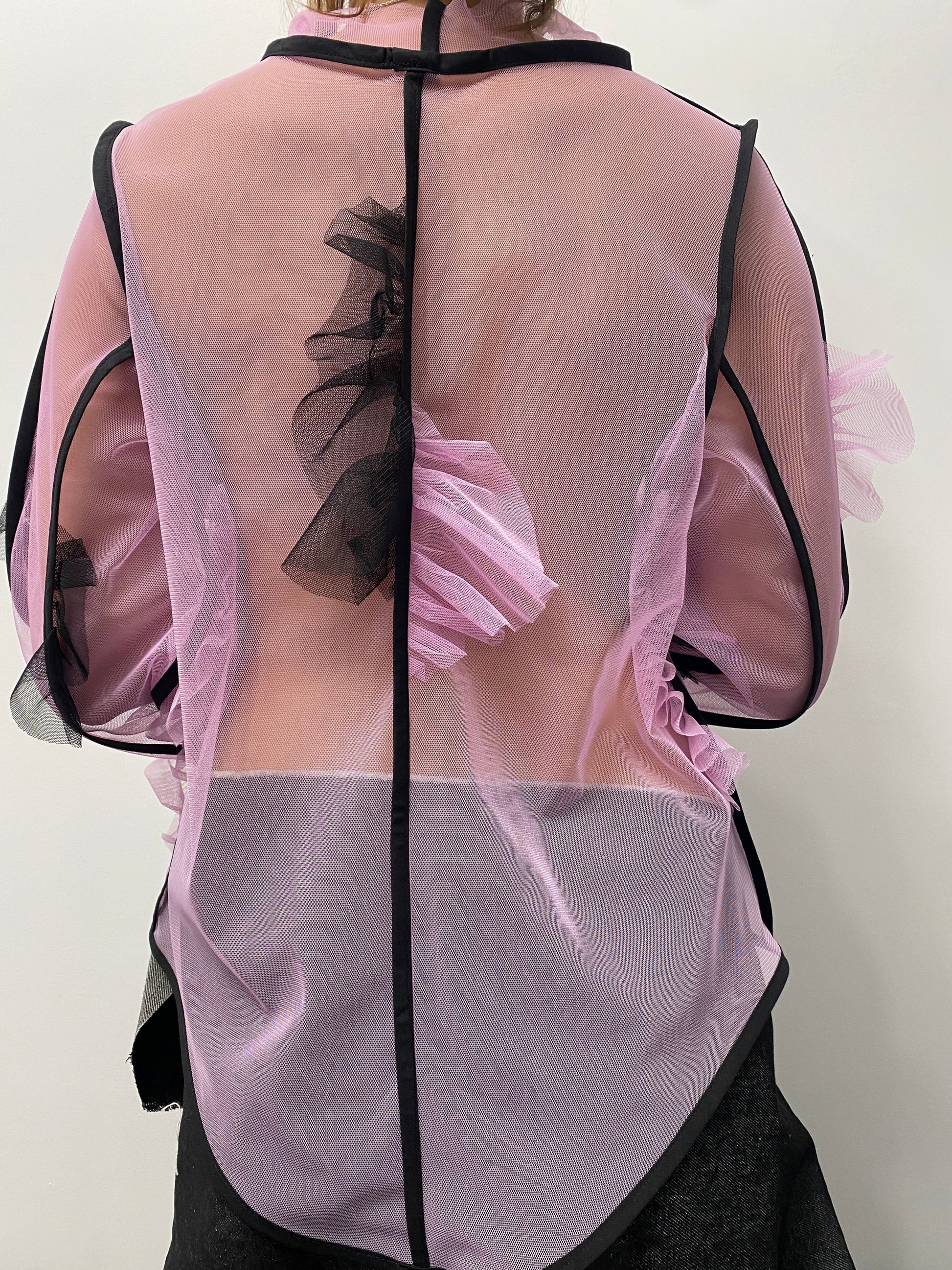 Partial view of a person wearing a sheer pink top with black straps on a white background