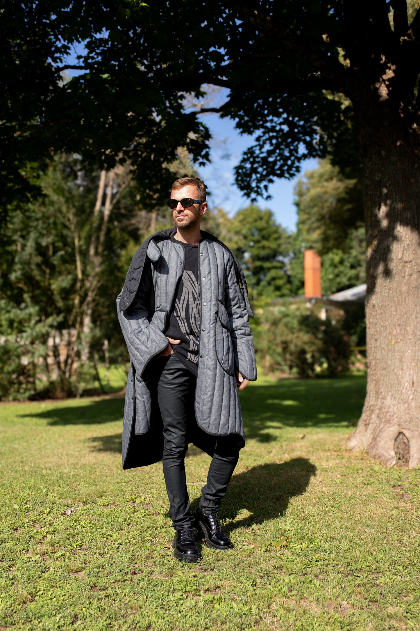 Man wearing a long grey Fronzi coat, it is sunny, so the coat is open