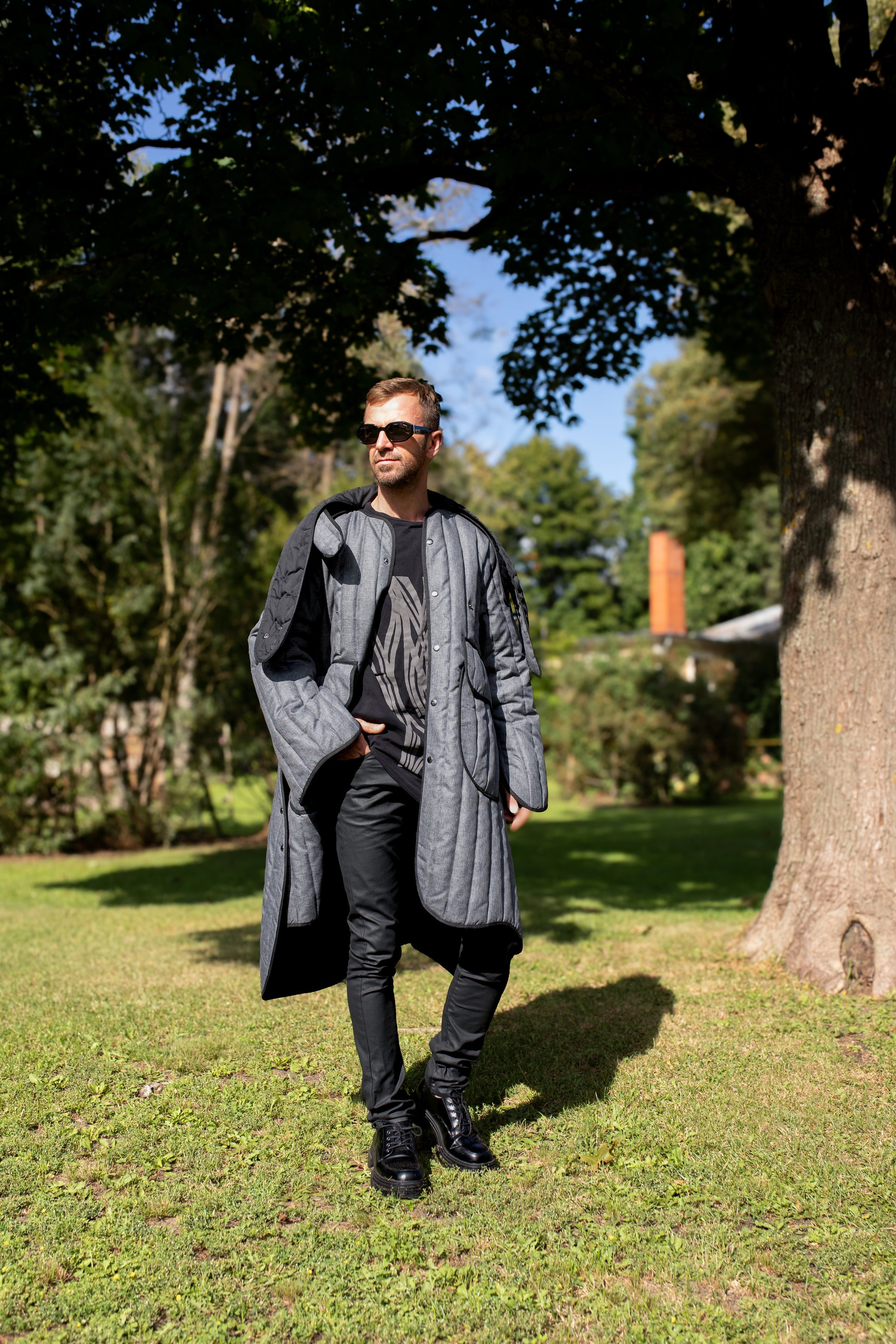 Man wearing a long grey Fronzi coat, it is sunny, so the coat is open