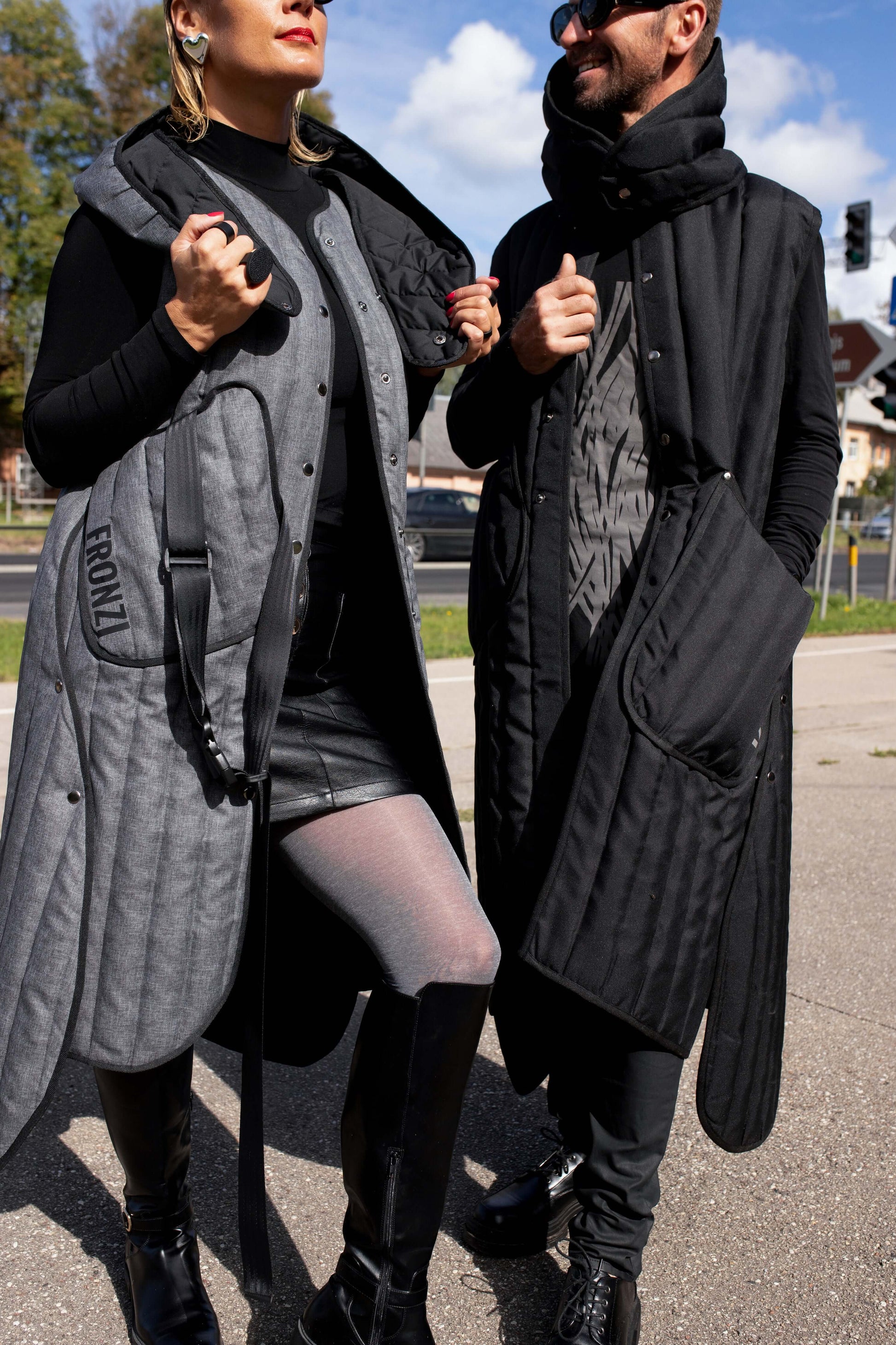 A man and woman both wearing long Fronzi vests, man is wearing a black vest and the woman is wearing a grey vest, they are in the sun, vests open