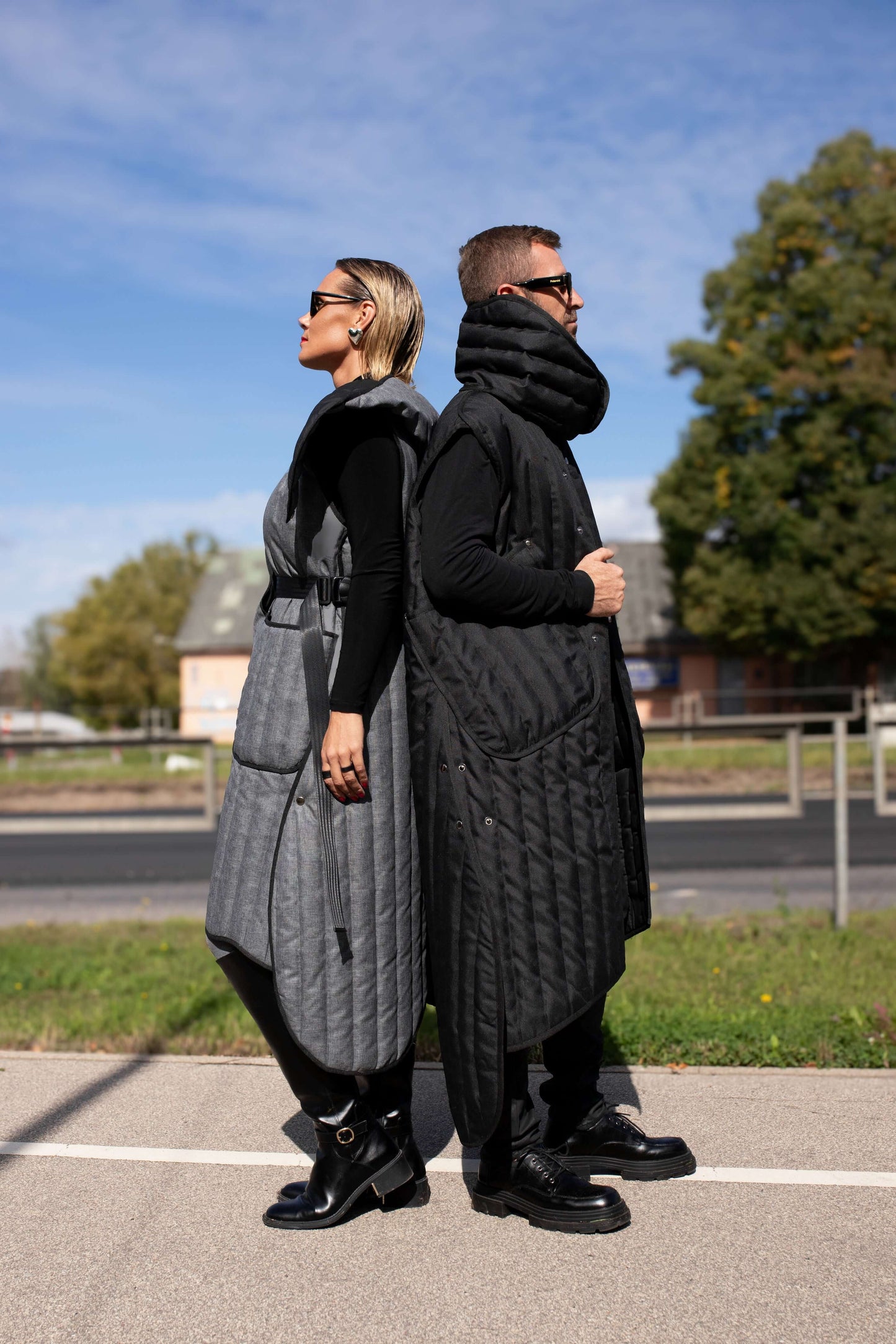 Man and woman standing with their backs to each other, both wearing Fronzi vests, one in grey and one in black