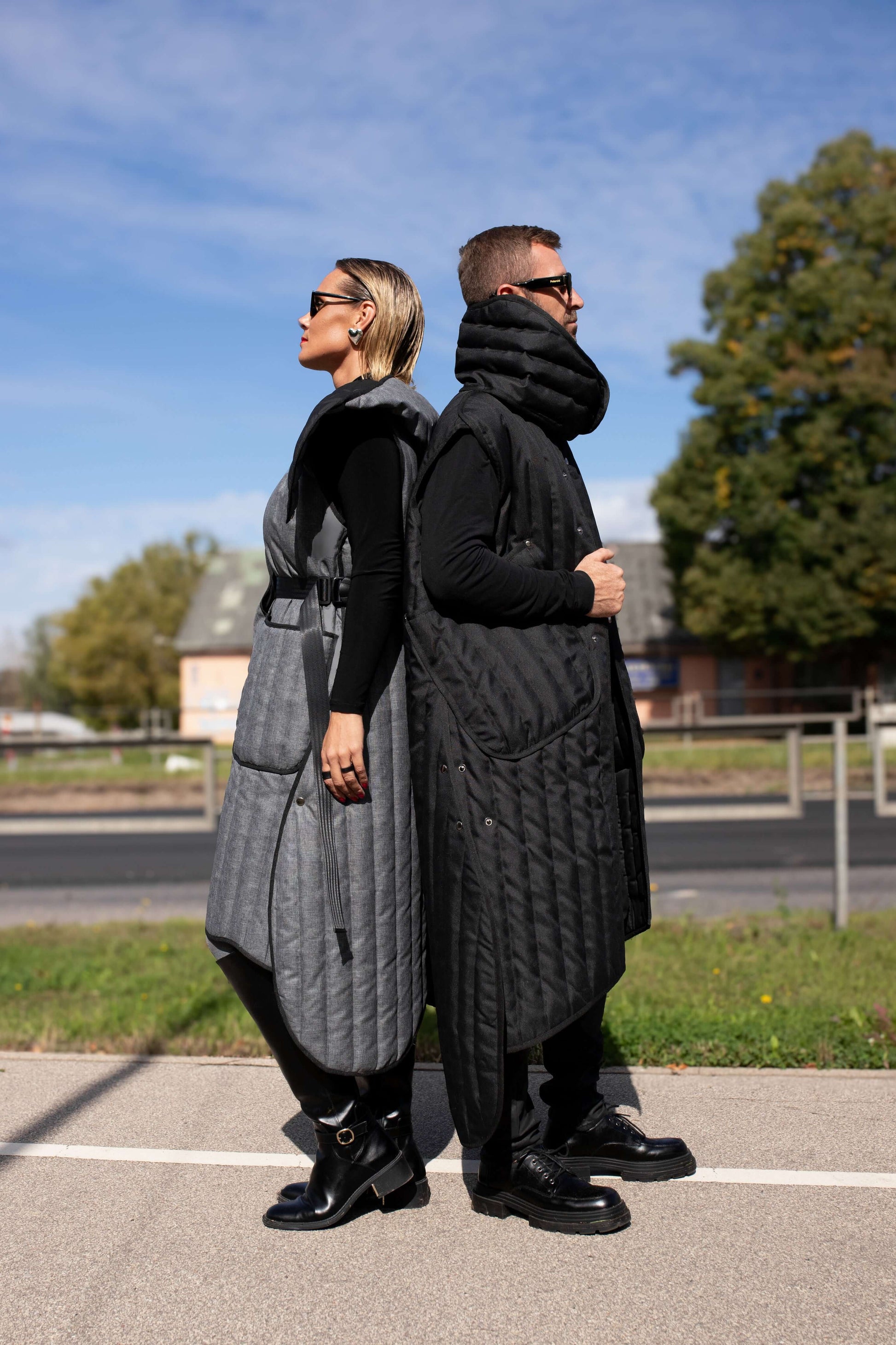 Man and woman standing with their backs to each other, both wearing Fronzi vests, one in grey and one in black