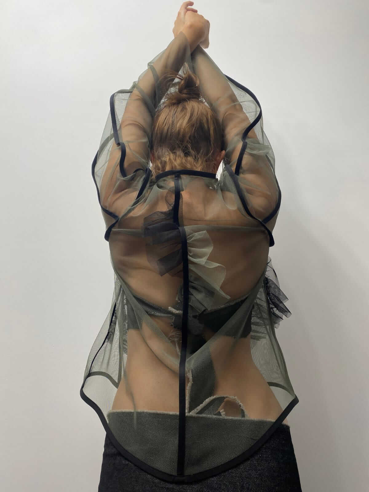 Model wearing khaki green see-through top with her arms help above her head