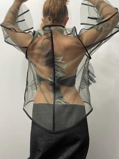 Model wearing a khaki green sheer top with black details and frills, from the back