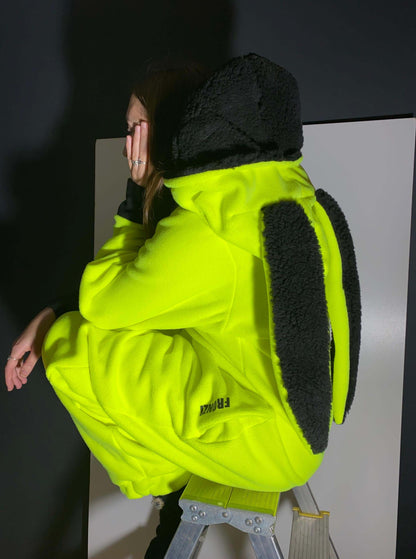 Model sitting on a ladder in a neon onesie with black long ears, side view