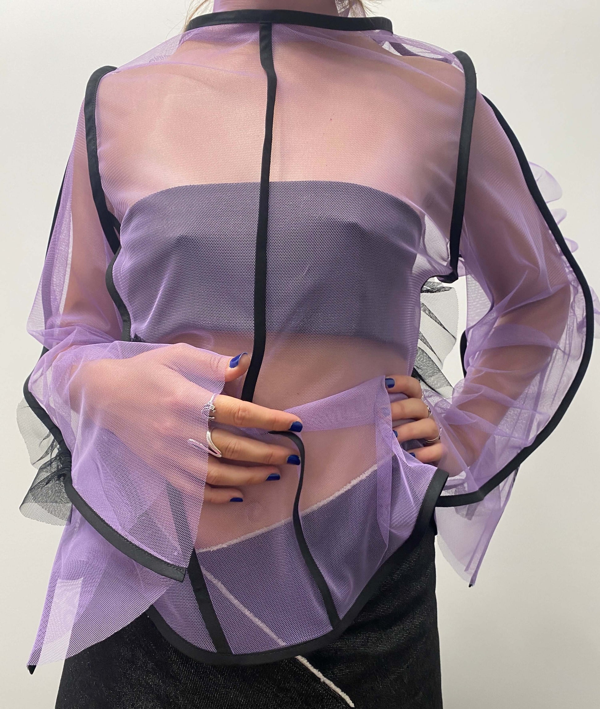 Model wearing a purple see-through top with black lines and frill details