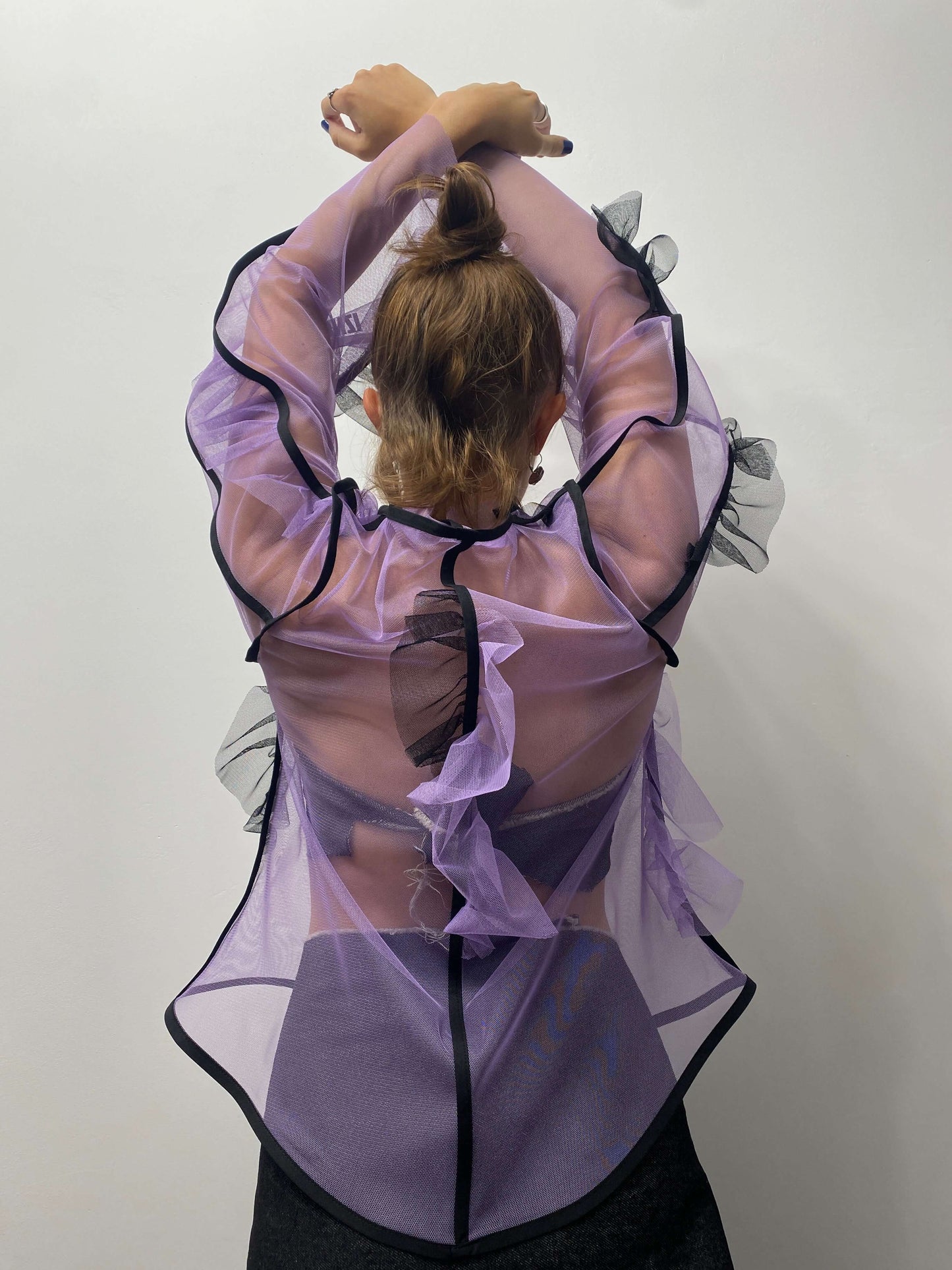 Model wearing purple sheer top with black details, from behind