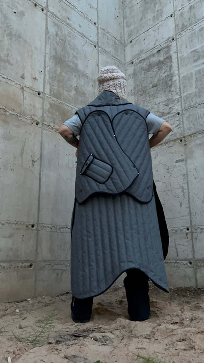 Back view of a model wearing a long gray coat and the removable sleeves attached to the back.