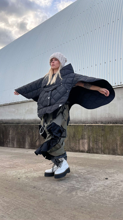 Side view of blond model wearing short quilted hooded jacket with arms wide open to show that this jacket is a transformer
