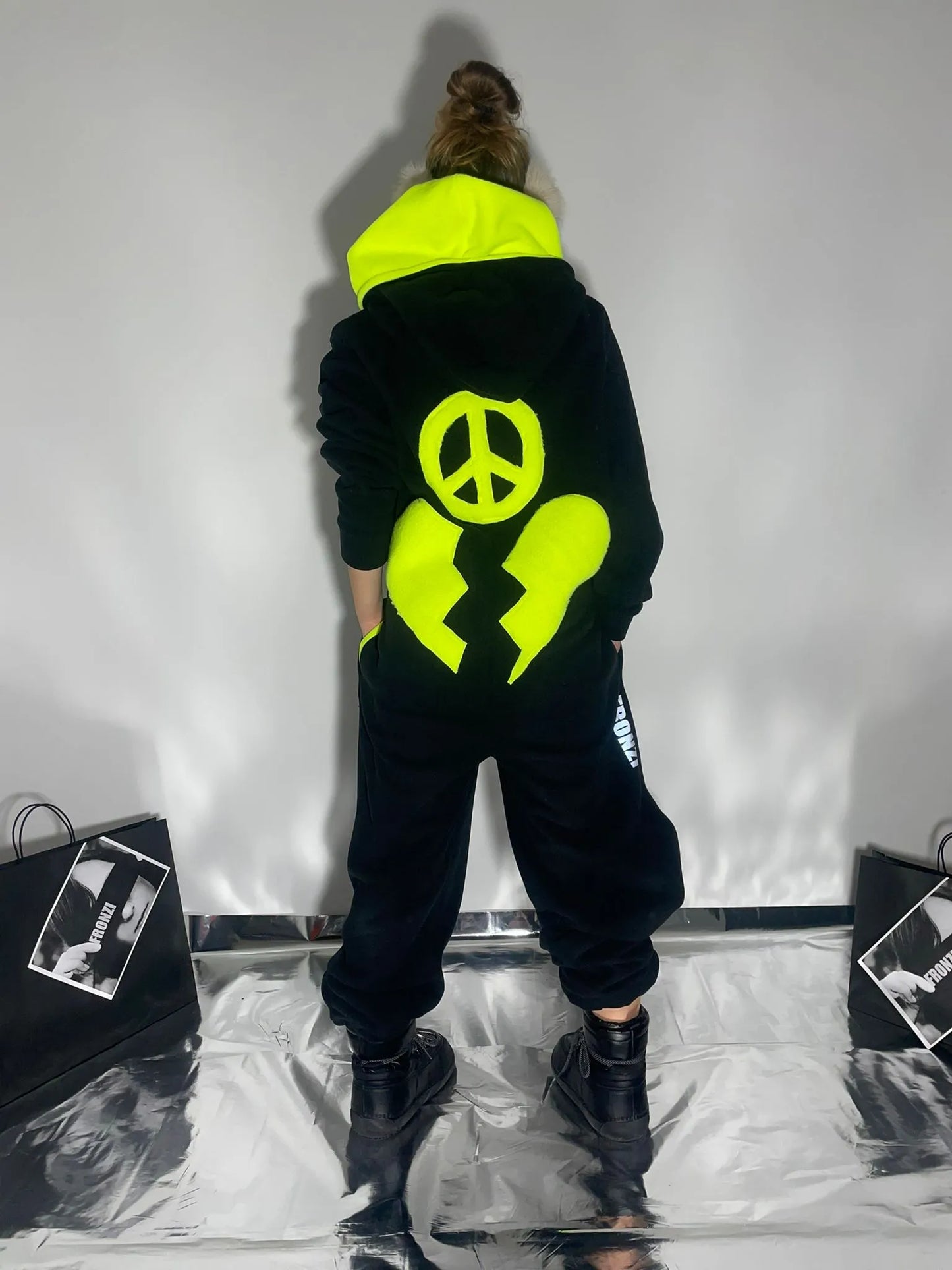 Model wearing a black fleece onesie with neon details on the back and a neon hood, view from the back