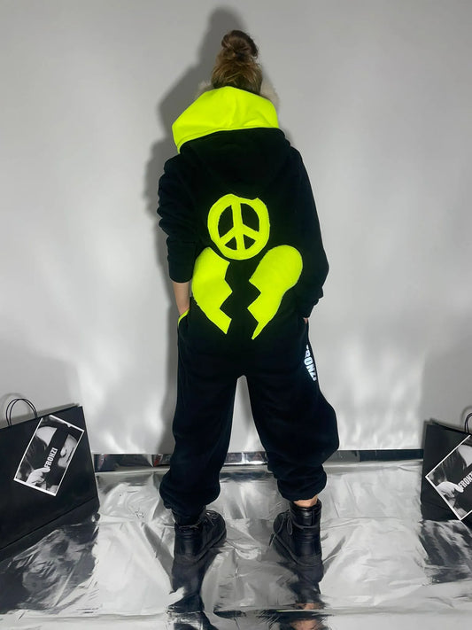 Model wearing a black fleece onesie with neon details on the back and a neon hood, view from the back