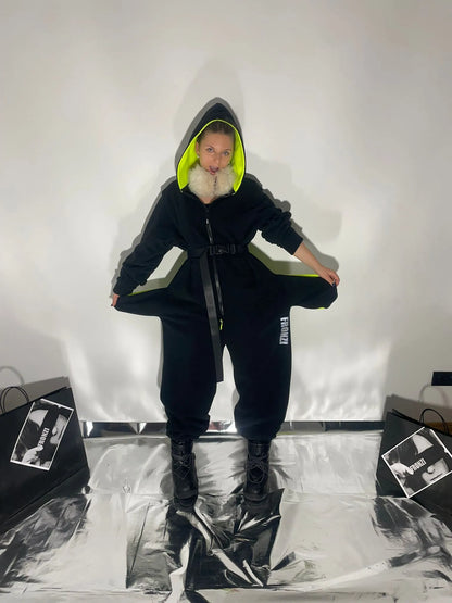 Model pulling out inside pockets of a black onesie that has neon and reflective details, view from the front