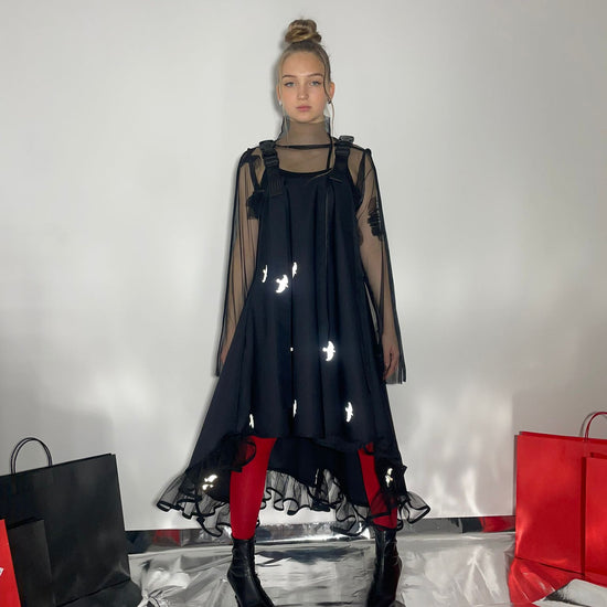 Video of model wearing a black dress with reflective birds with a Fronzi bag in her hands and then walking away form the shot